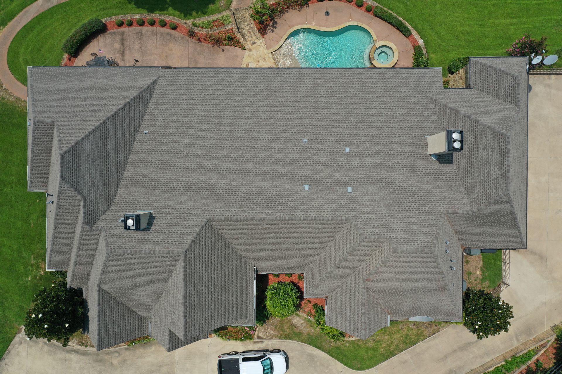 Aerial view of a gray-roofed suburban house with a backyard pool and lawn.