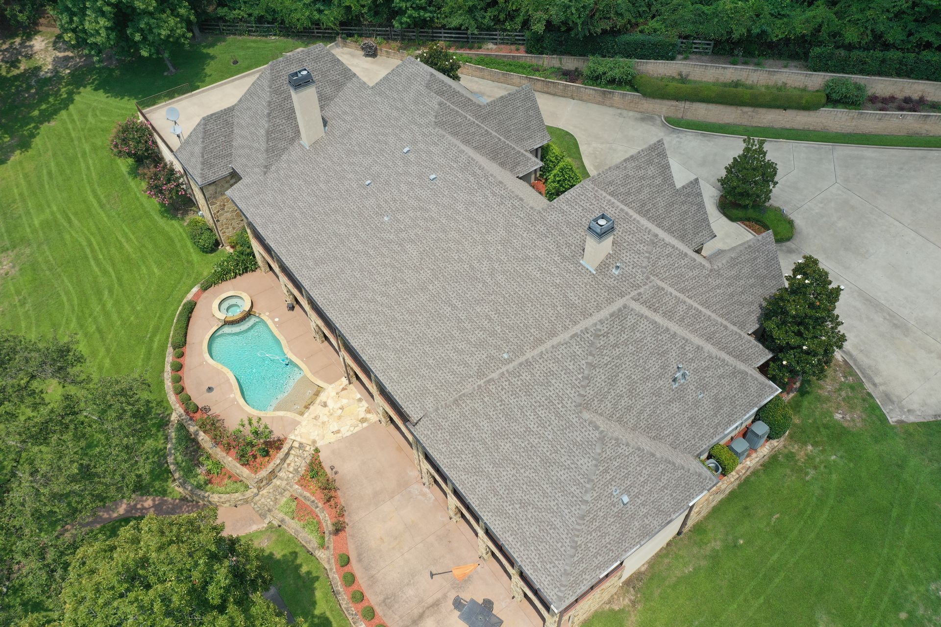 Aerial view of a large gray-roofed house with a backyard pool and surrounding green lawn