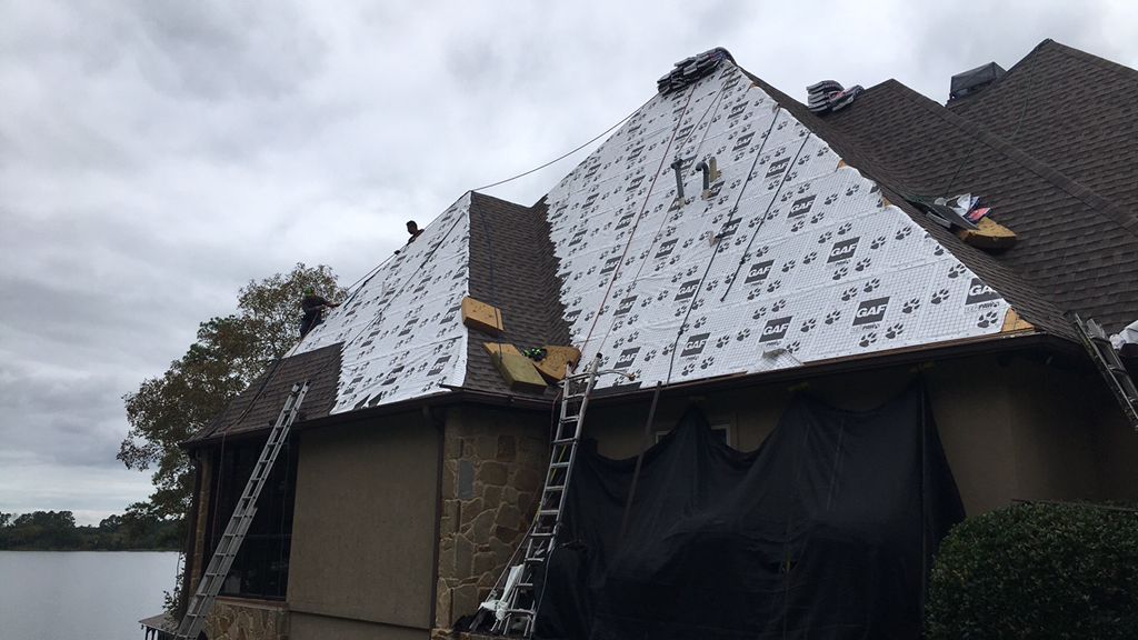 Damaged roof with torn white tarp and ladders leaning against a house under cloudy skies