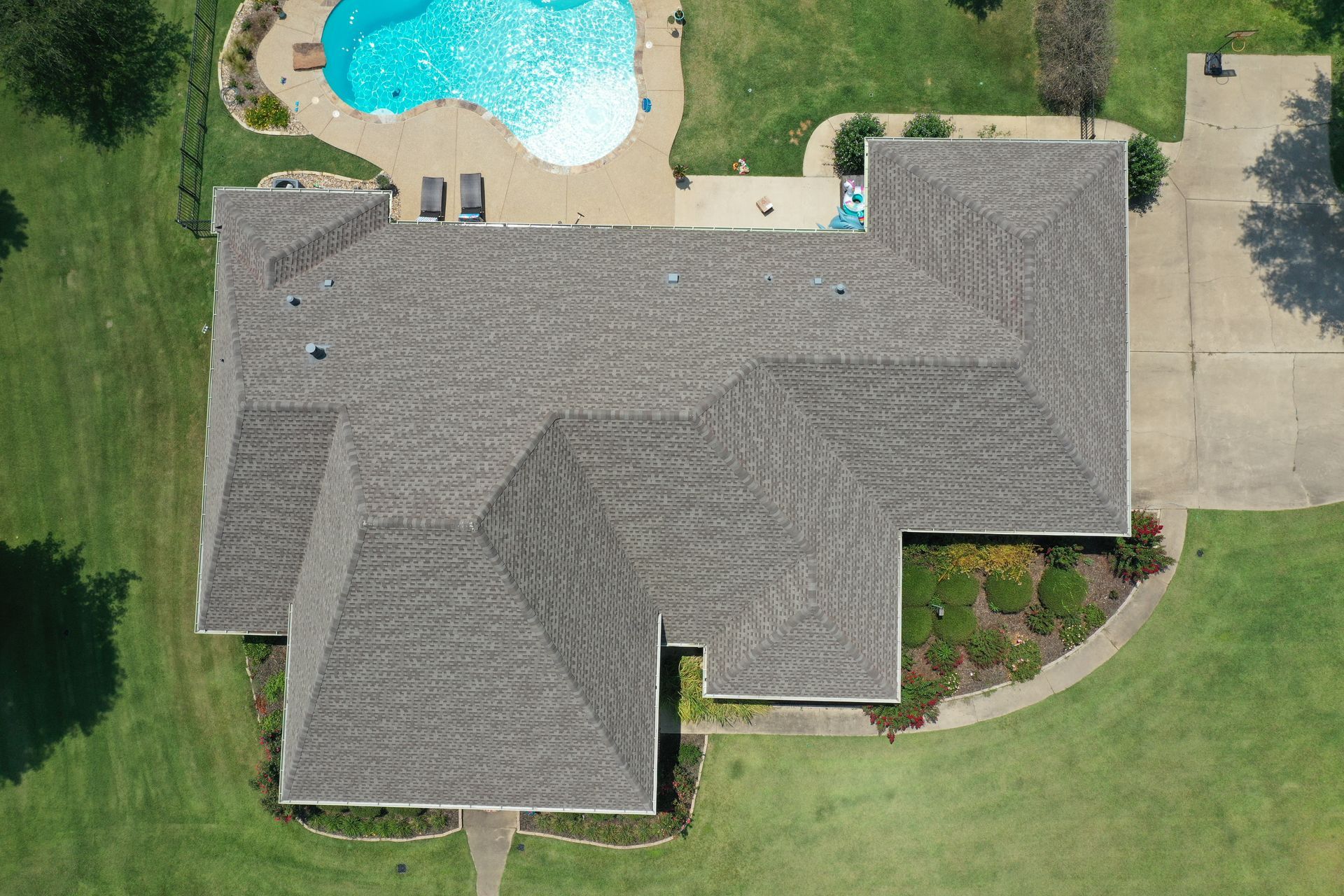 Aerial view of a suburban house with gray roof, backyard pool, and green lawn.