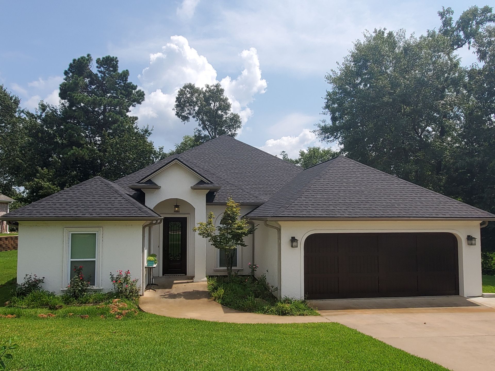 Single-story suburban house with a dark roof, two-car garage, and landscaped front yard under a blue sky