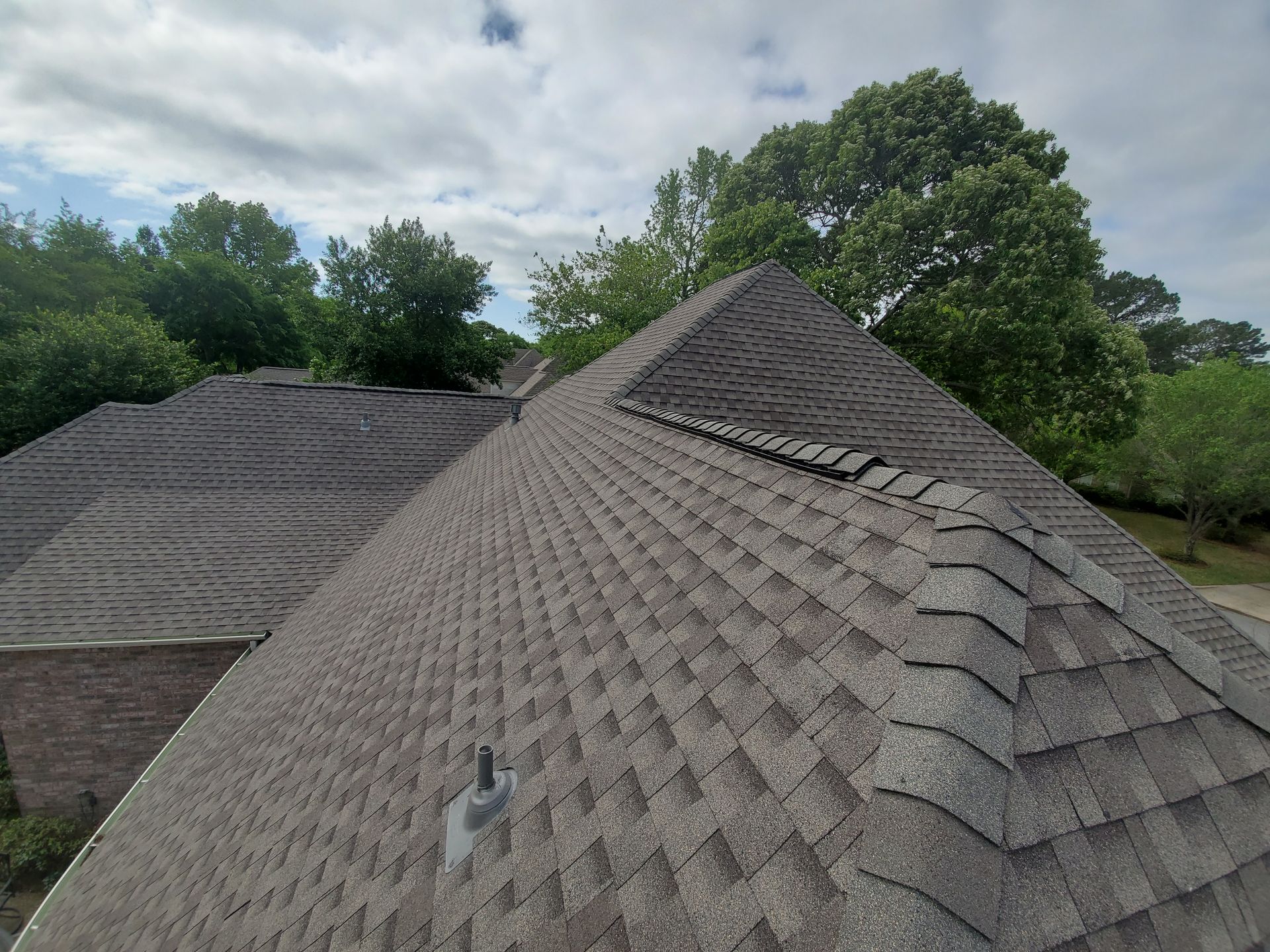 Gray shingled roof with a steep peak under a cloudy sky, with trees in the background