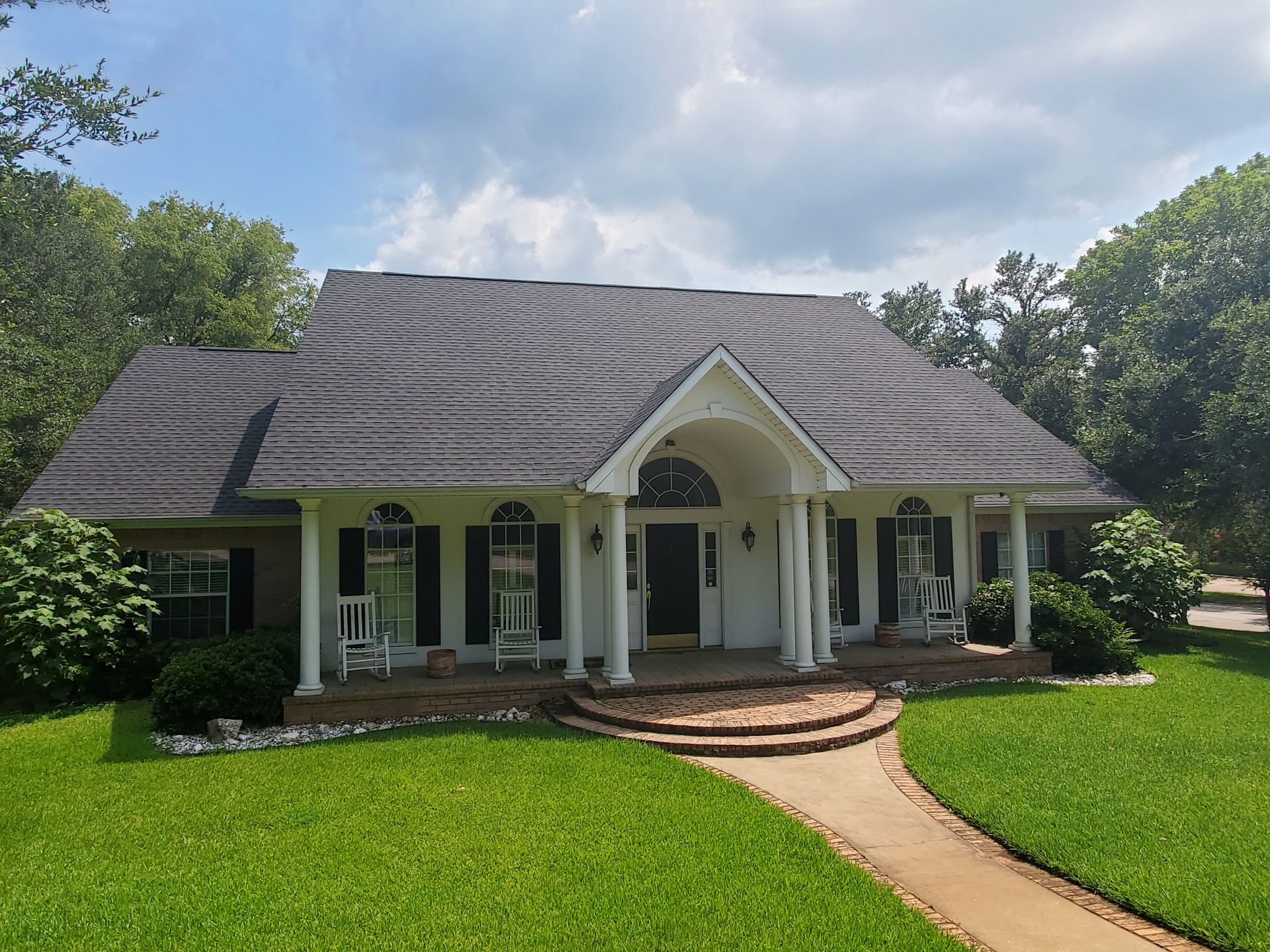 Single-story white house with dark roof, arched porch, and curved walkway in a green yard