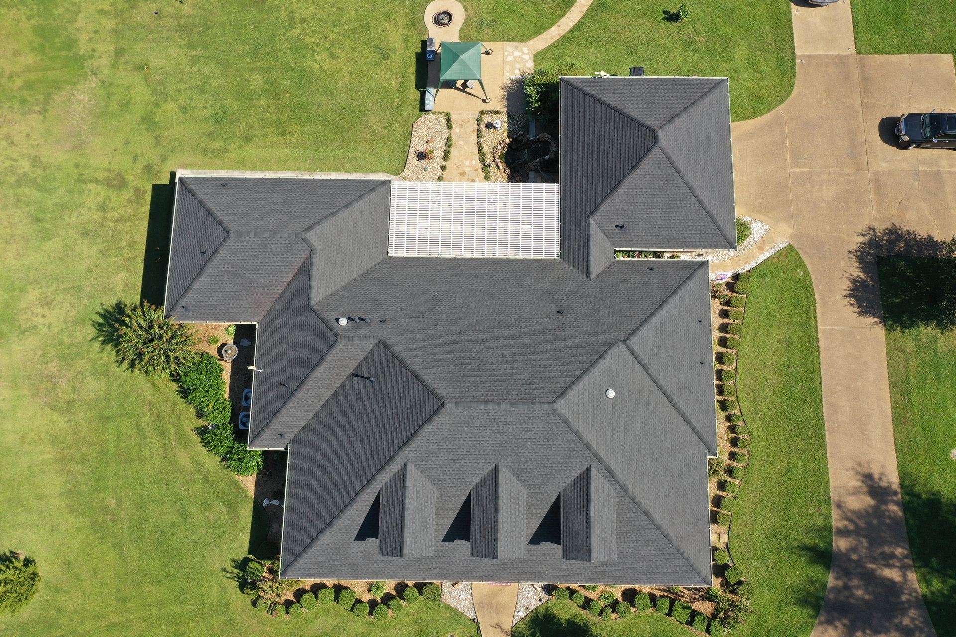 Aerial view of a house with a dark gray roof, backyard patio, and driveway on a grassy lot