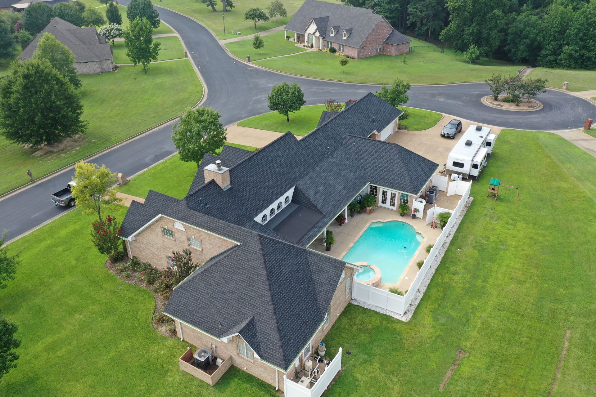 Aerial view of a large suburban house with a backyard pool, driveway, and surrounding green lawn.