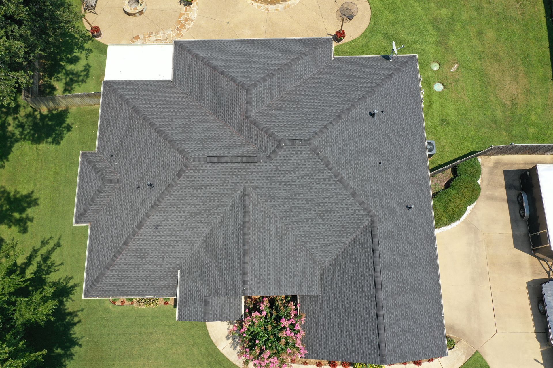 Aerial view of a dark gray shingled house roof with lawn, driveway, and patio visible շուրջ