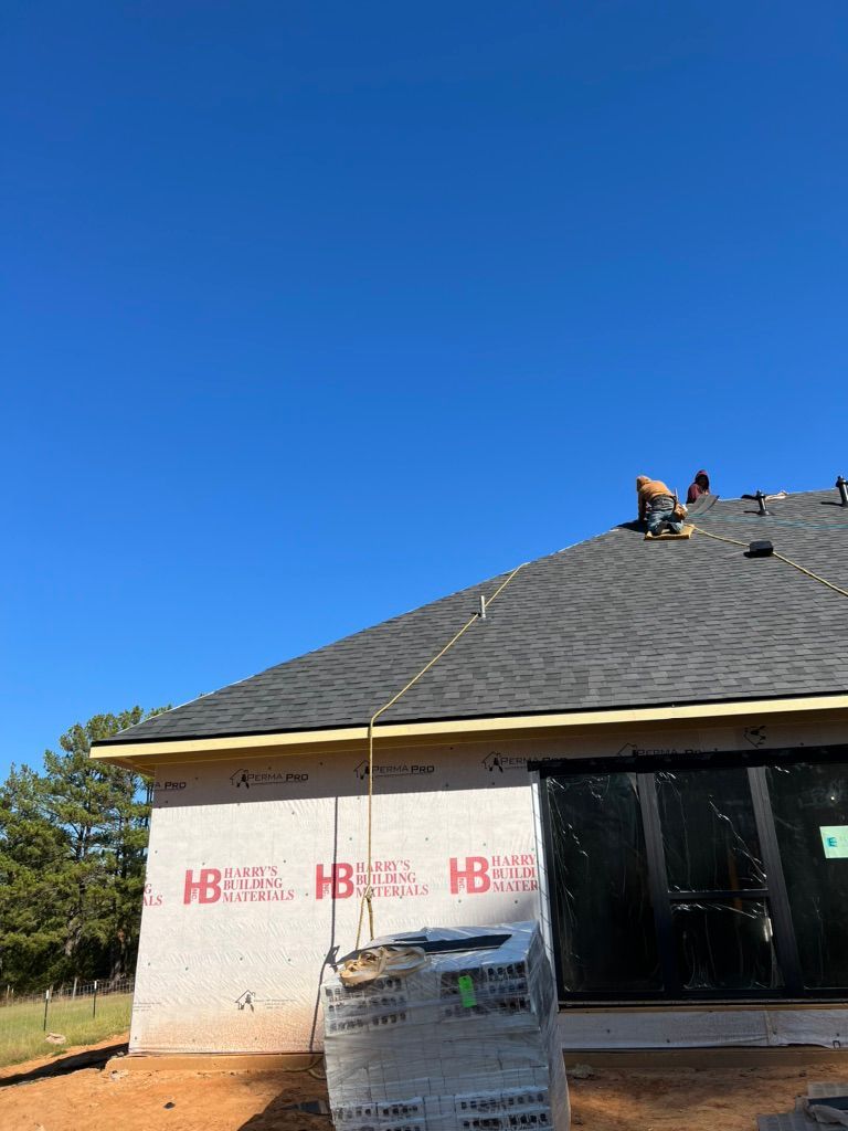 House under construction with workers on the roof, gray shingles, and blue sky.