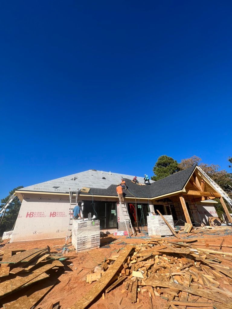 Partially built house with exposed roof framing and piles of lumber under a clear blue sky