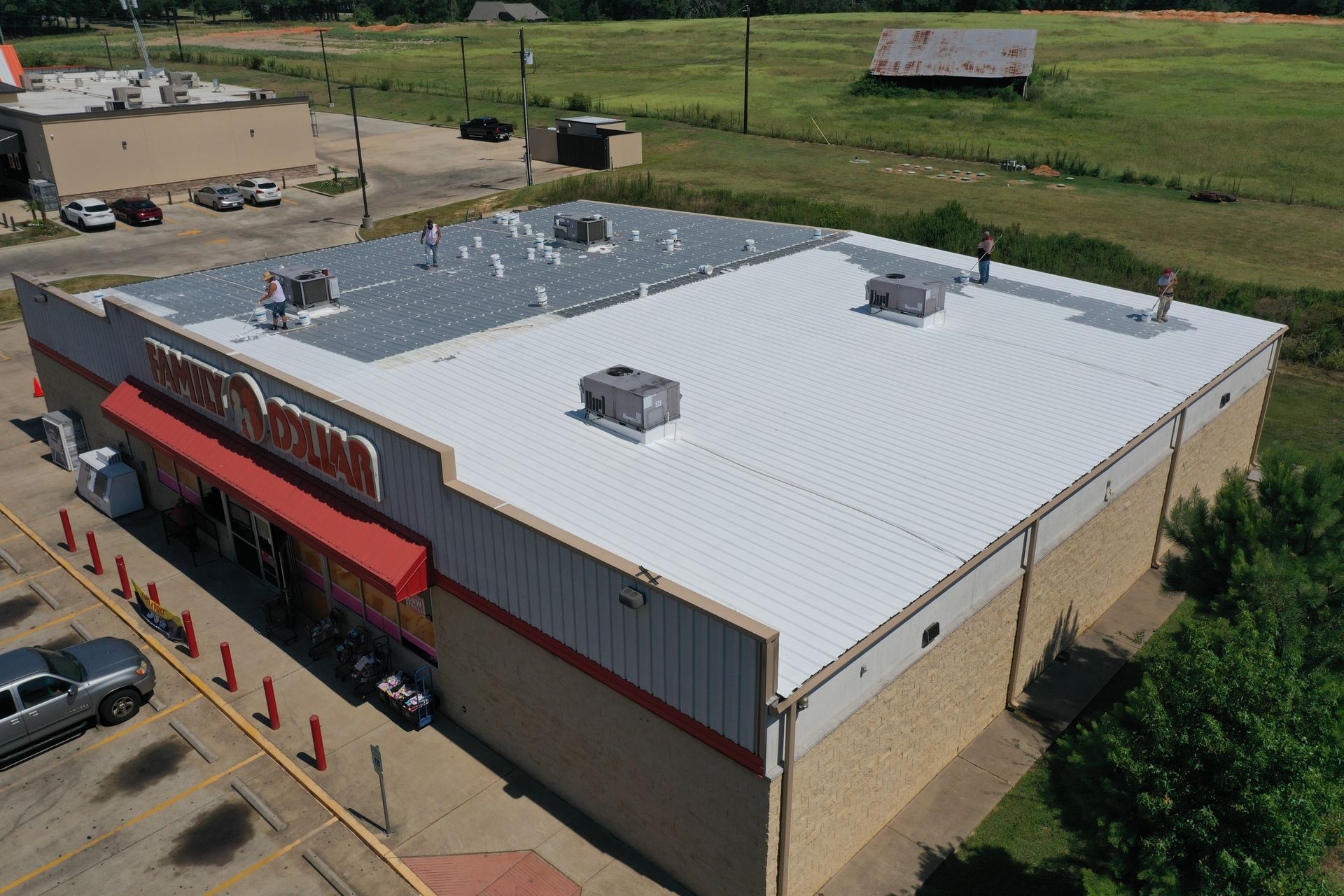 Aerial view of a large red-and-beige commercial building with a white roof and parked cars outside