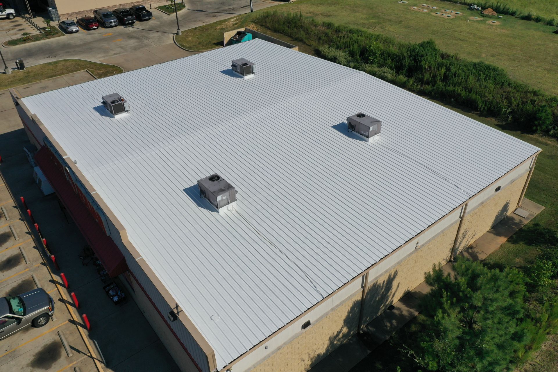 Aerial view of a large beige industrial building with a white metal roof and four rooftop vents.