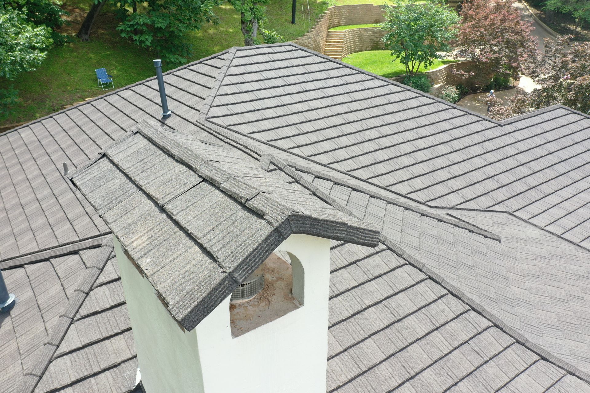 Damaged gray shingle roof with a missing section around a white chimney, viewed from above