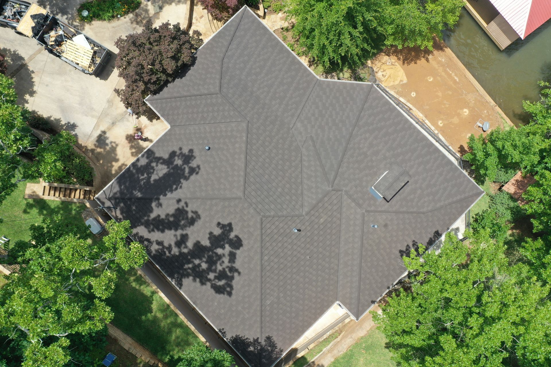 Aerial view of a house with a dark gray roof surrounded by trees and a driveway.