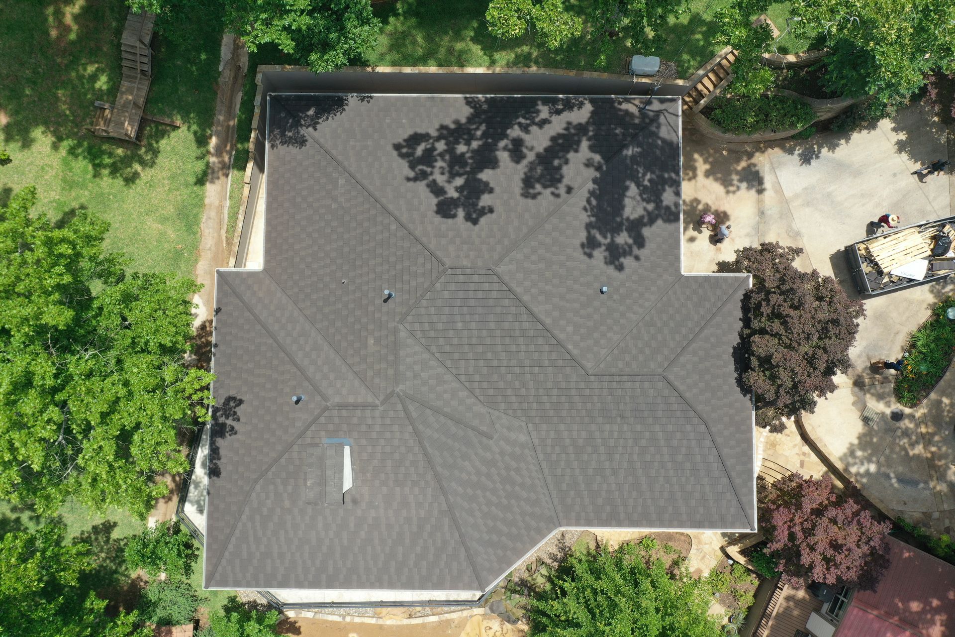 Aerial view of a gray-roofed house surrounded by green trees and landscaping.