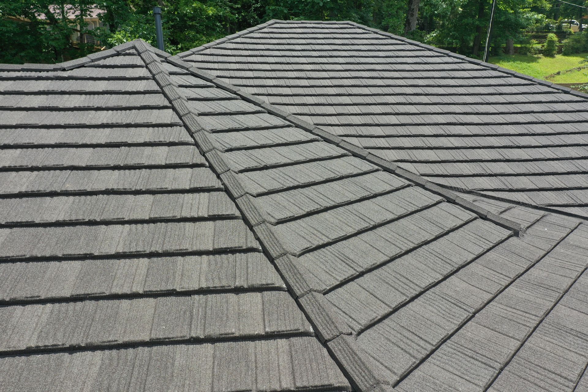 Gray shingle roof with intersecting ridgelines and a textured pattern against green trees