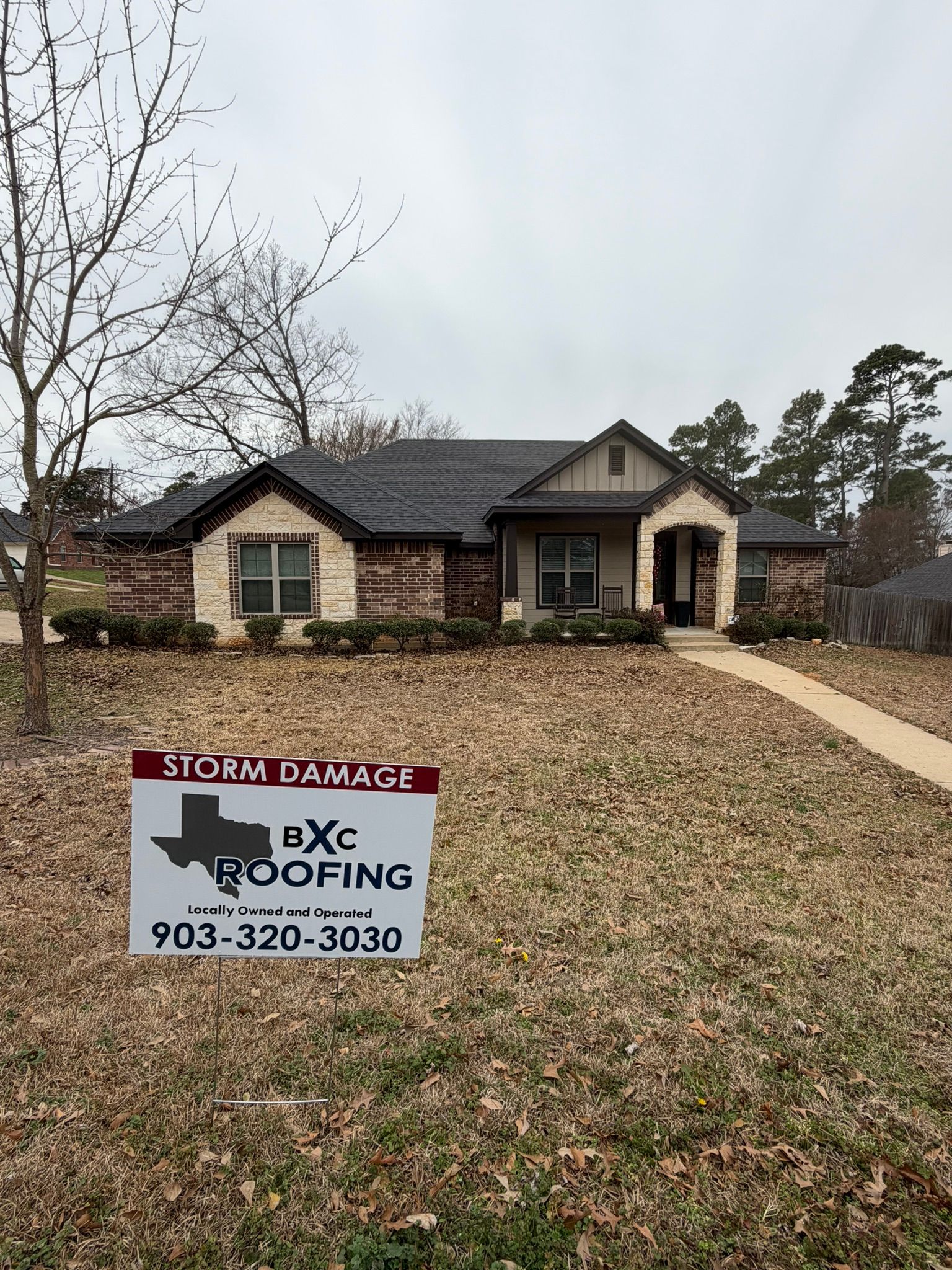 Front yard sign for a roofing company in front of a suburban house with brick and stone exterior