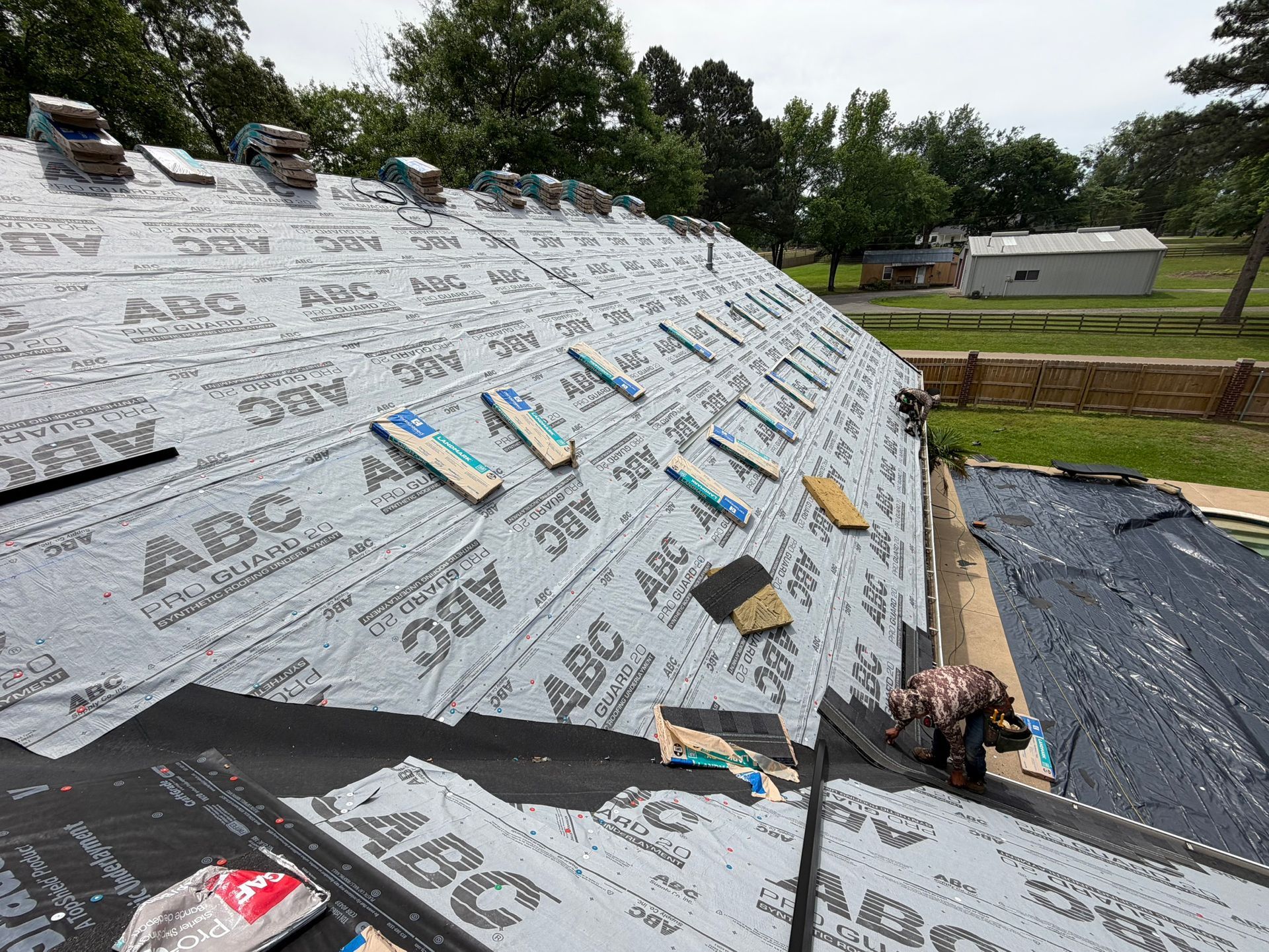 Roof under construction with roofing underlayment, scattered tools, and a worker near the edge