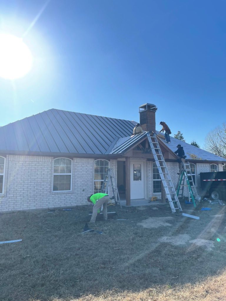 Worker on a ladder repairing a roof on a stone house in bright sunlight