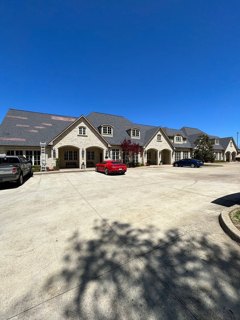 Row of beige townhouses with parked cars under a clear blue sky, viewed across a sunny driveway