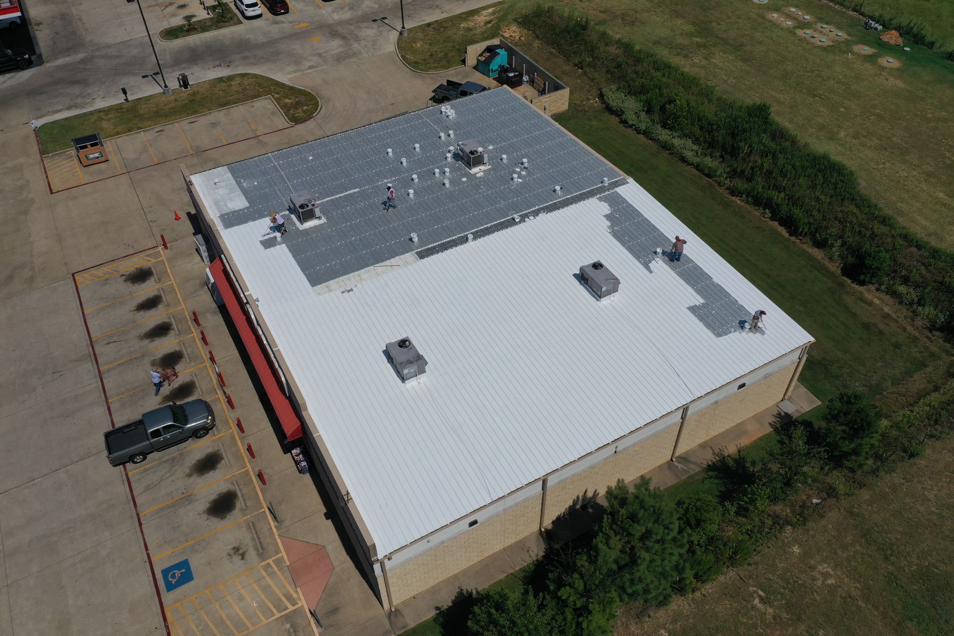 Aerial view of a large beige building with a white roof, gray rooftop section, and parking lot beside it