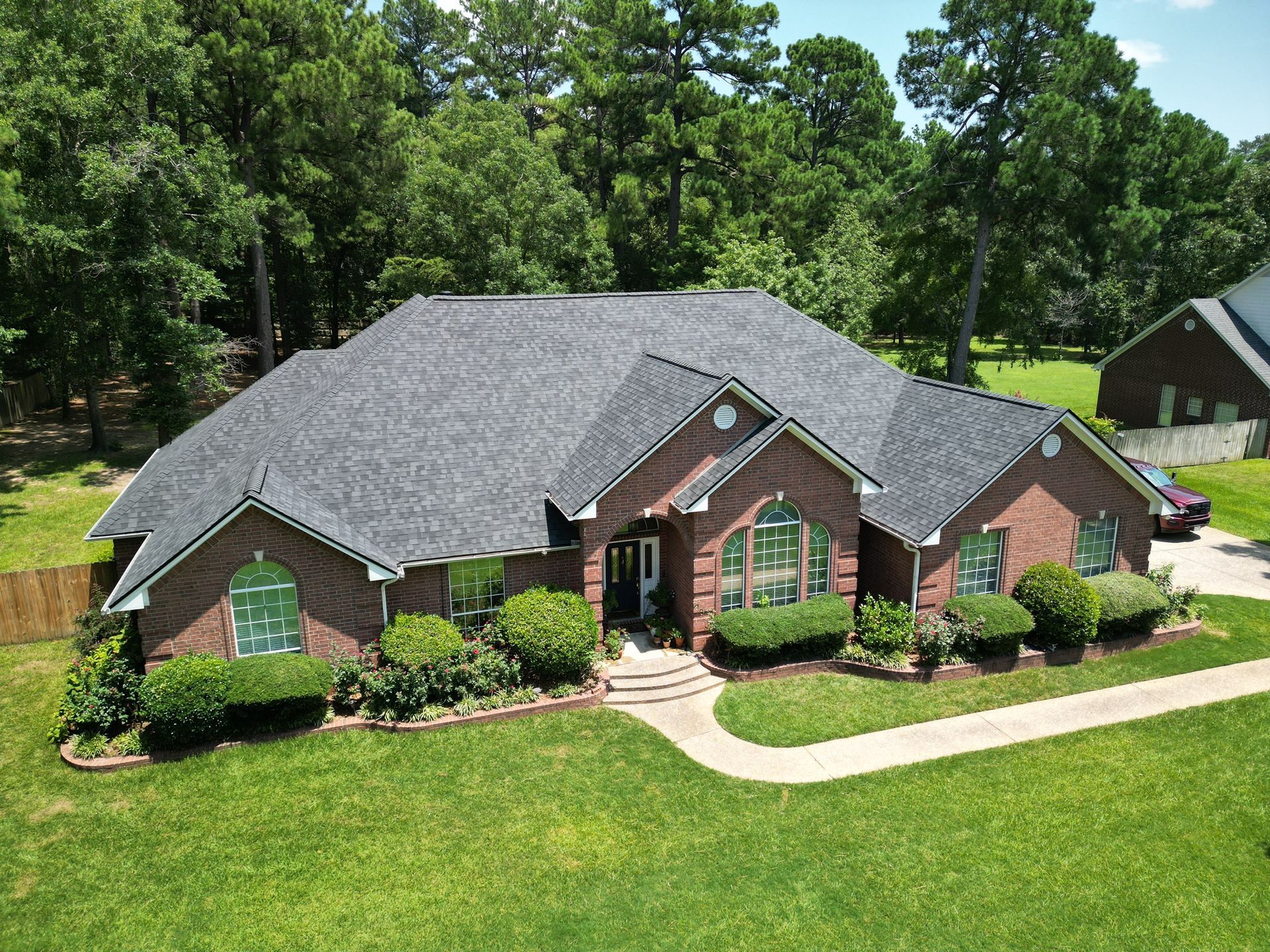 Brick suburban house with gray roof, green lawn, and trees in the background