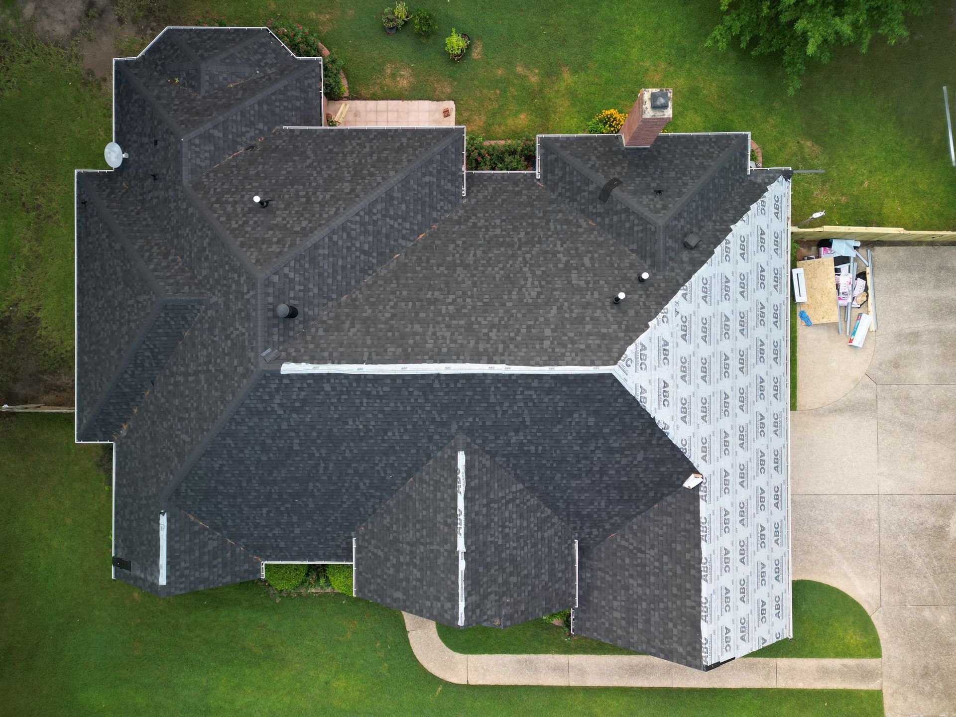 Aerial view of a large dark-roofed house with a light-sided section, driveway, and surrounding lawn.