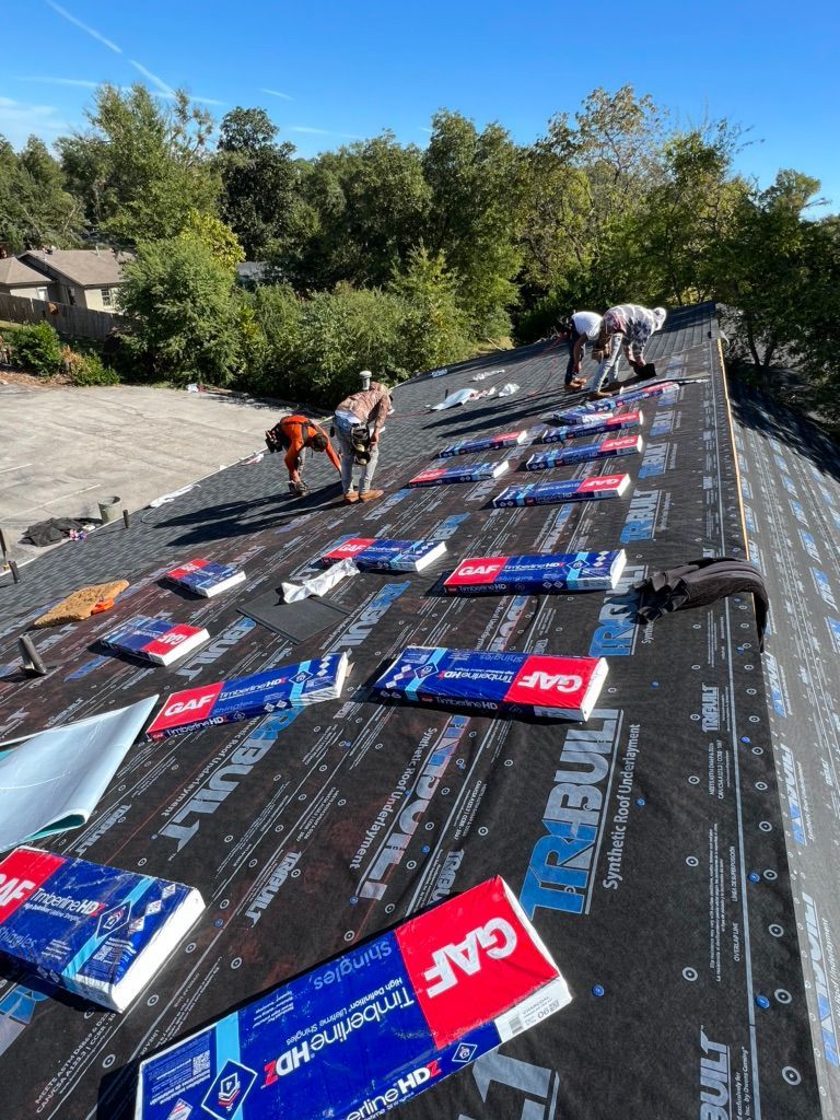 Workers installing roofing shingles on a sloped roof under a clear sky