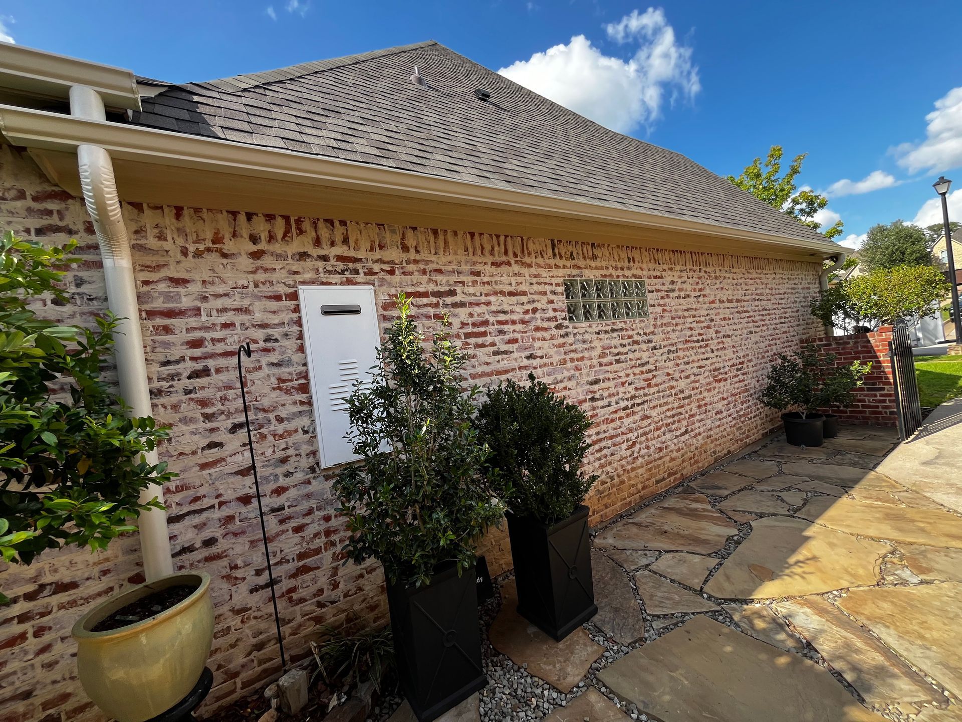 Brick house exterior with a white door, potted plants, and a stone walkway under a cloudy sky