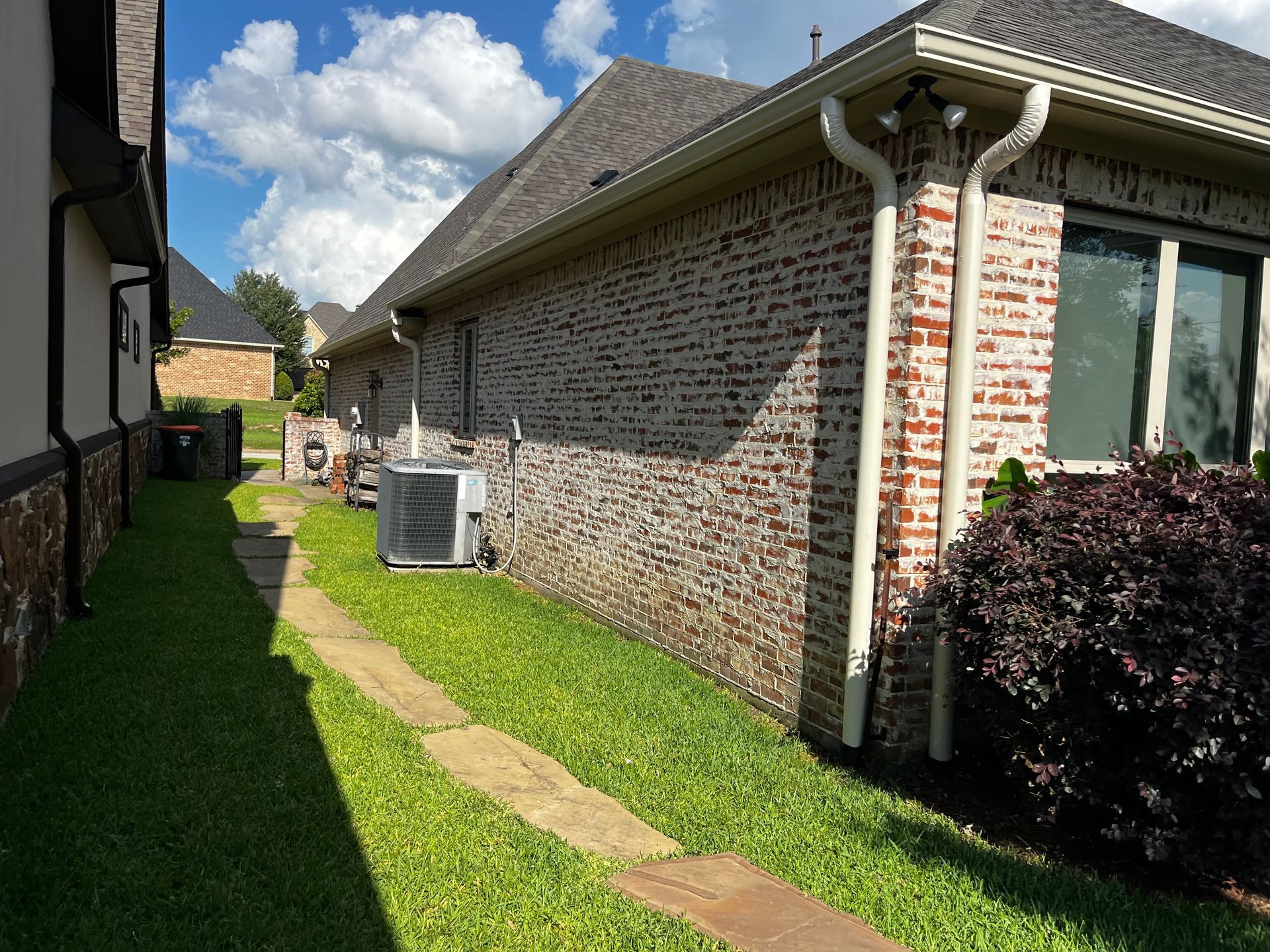 Brick house side yard with green lawn, narrow walkway, and cloudy blue sky