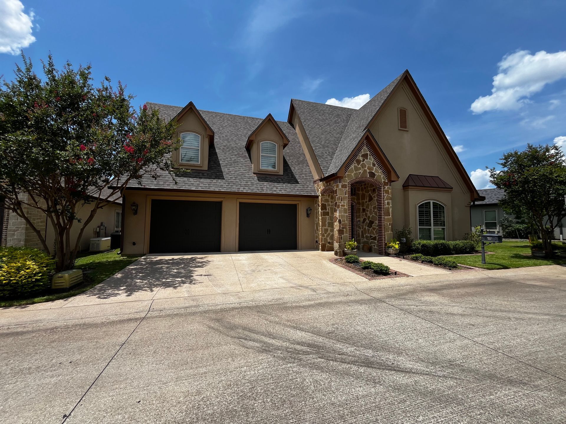 Suburban house with two-car garage, stone accents, and a gravel driveway under a blue sky.