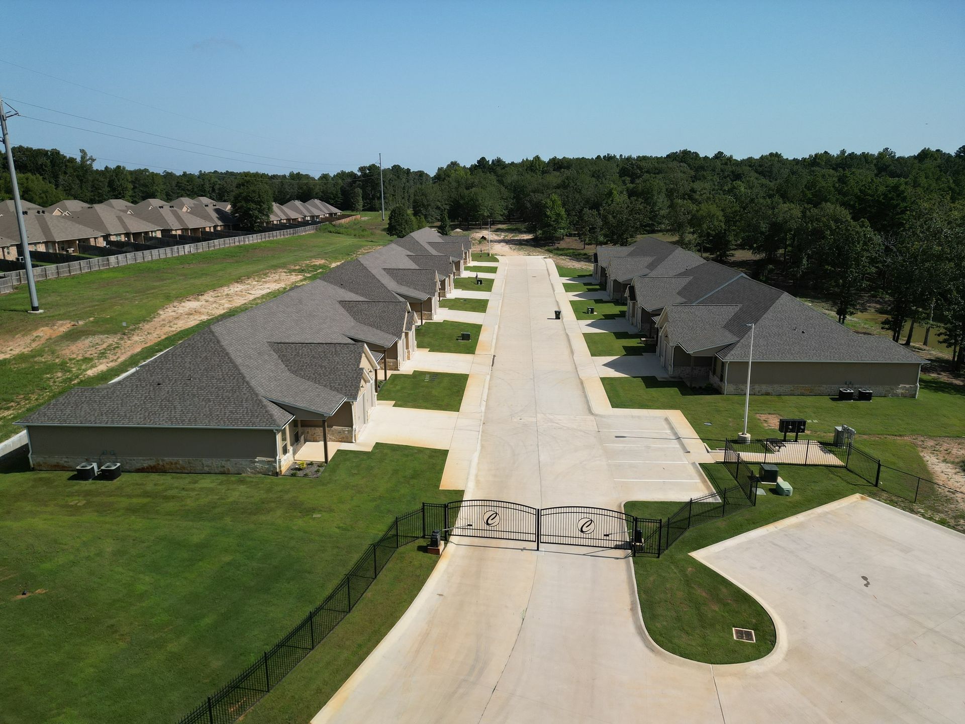 Aerial view of a suburban street with rows of houses and green lawns under a clear blue sky