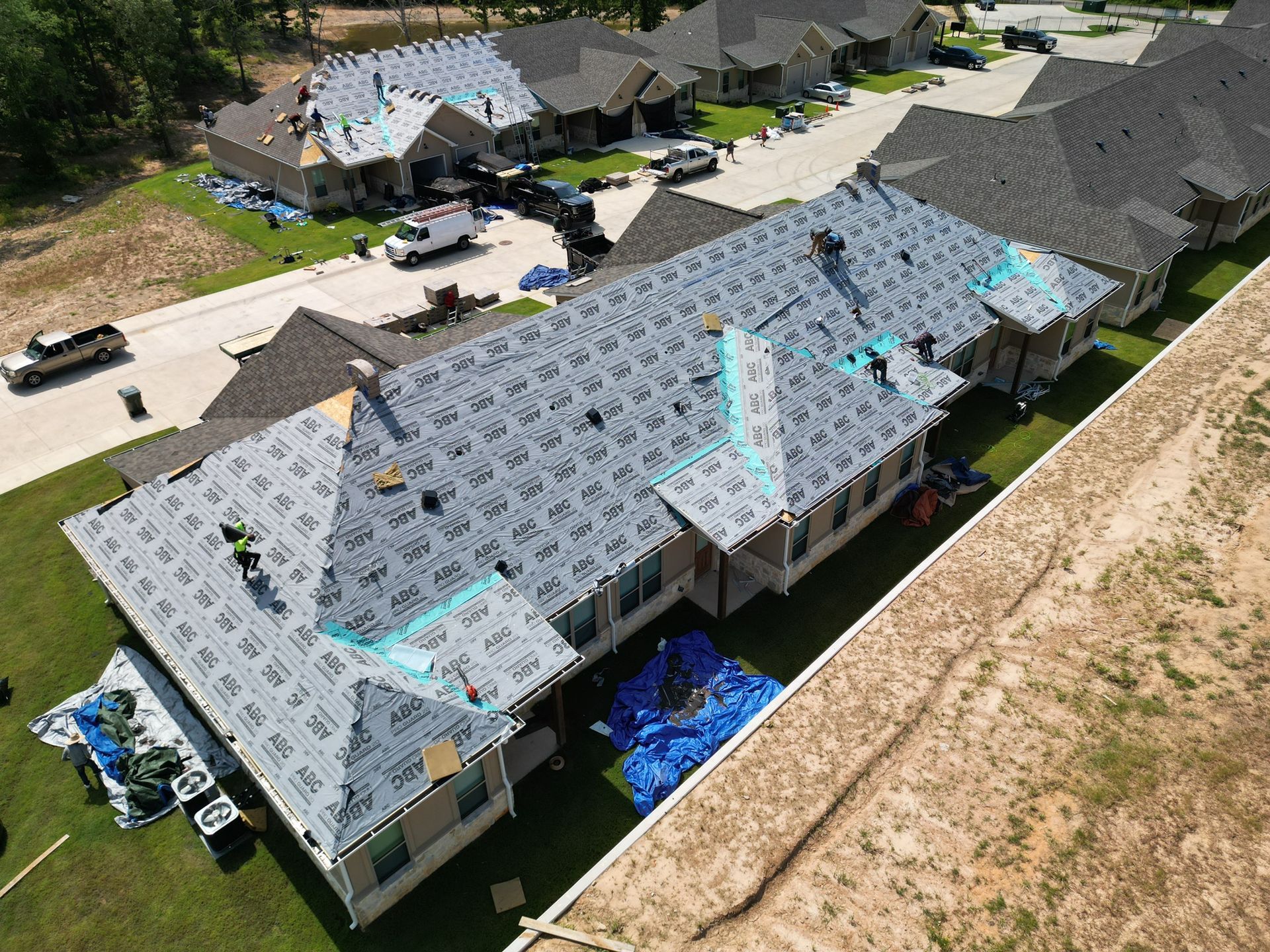 Roofing workers on a townhouse complex, with a gray roof under construction and blue tarps below