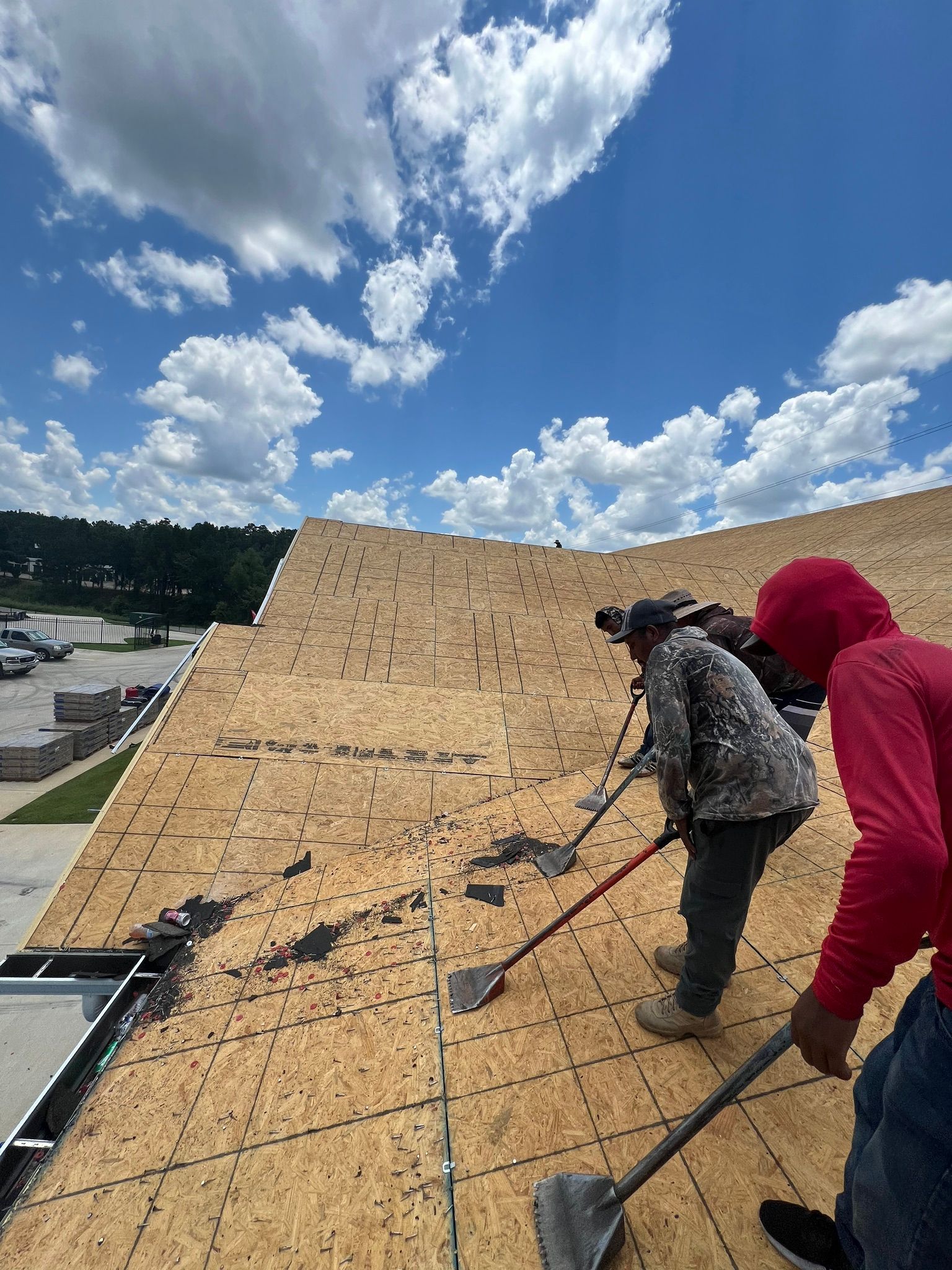Workers roofing a house under a blue sky, laying wooden shingles on a steep roof.