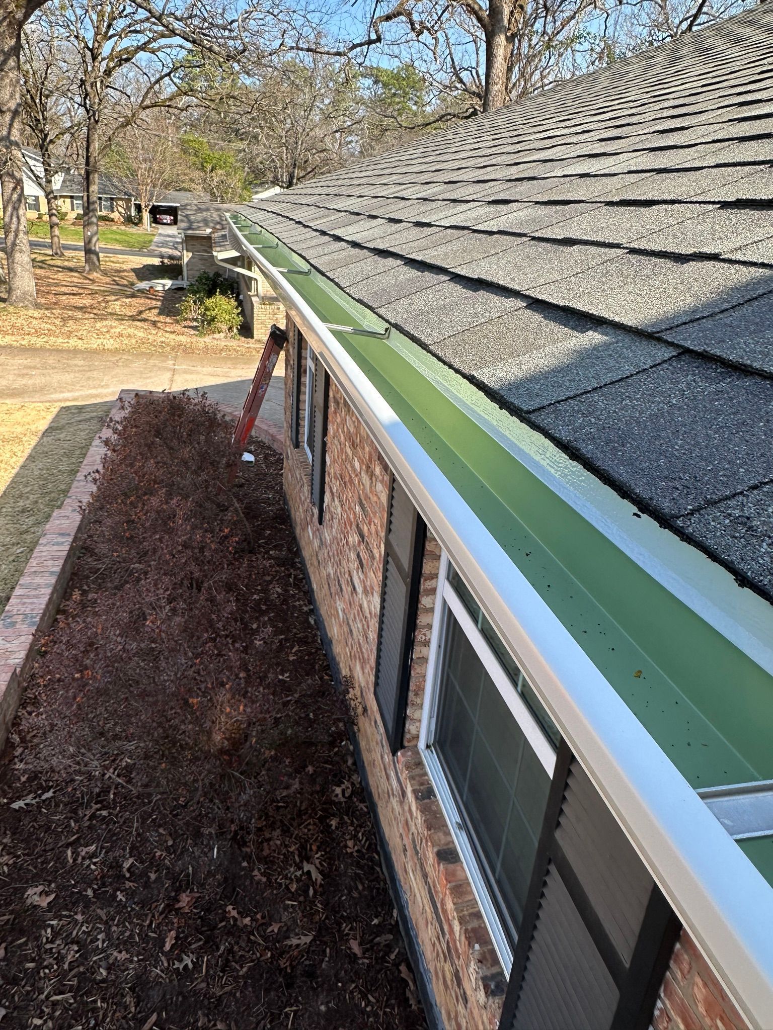 Brick house roof with white gutter and mossy shingles, viewed from the eaves along a side yard