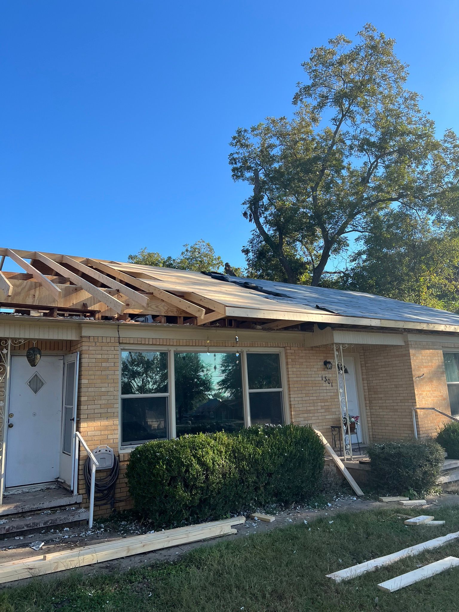Damaged house with roof missing and broken windows after storm, under a clear blue sky