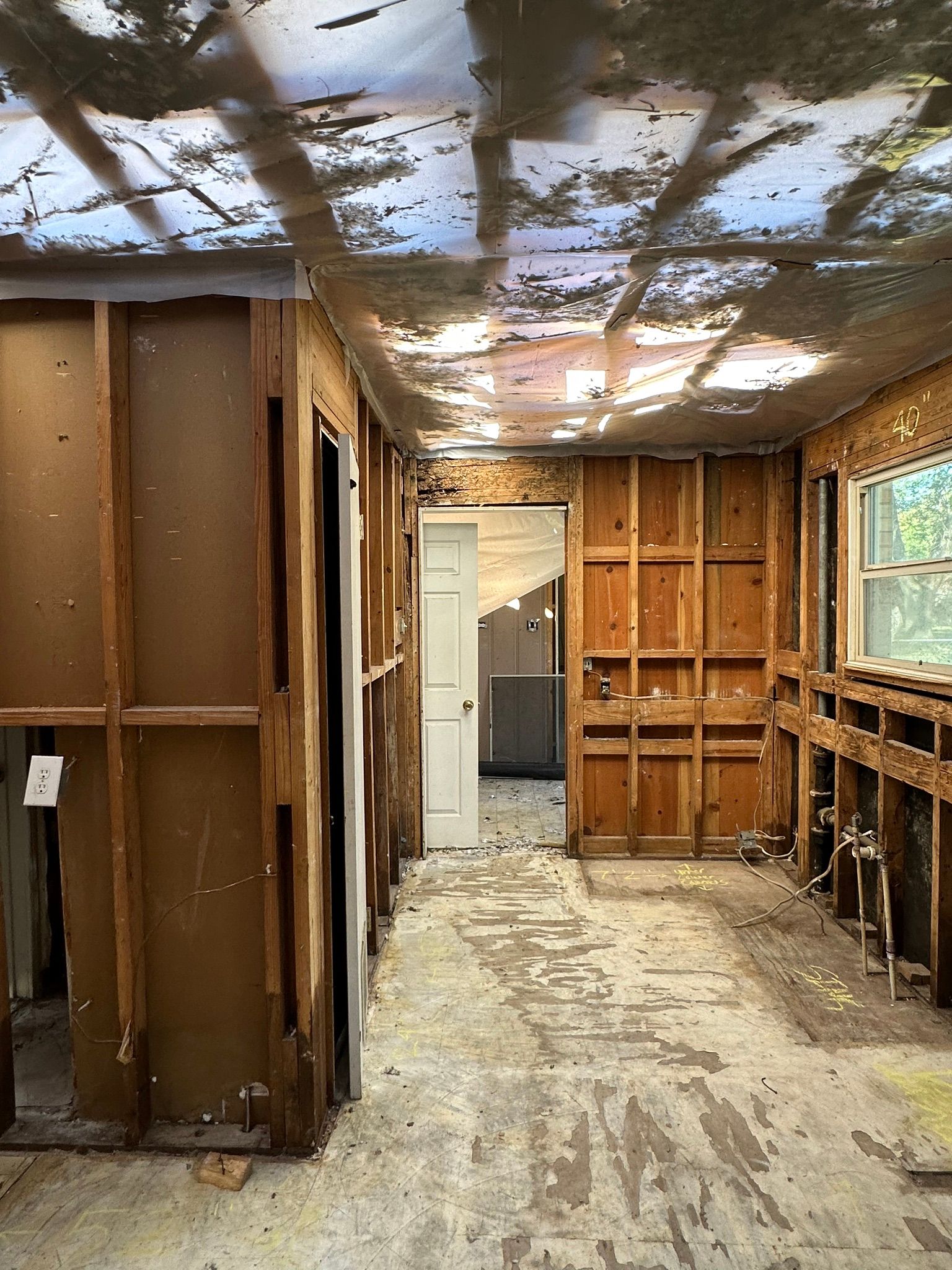 Interior of a room under renovation with exposed studs, debris-covered floor, and damaged ceiling insulation.
