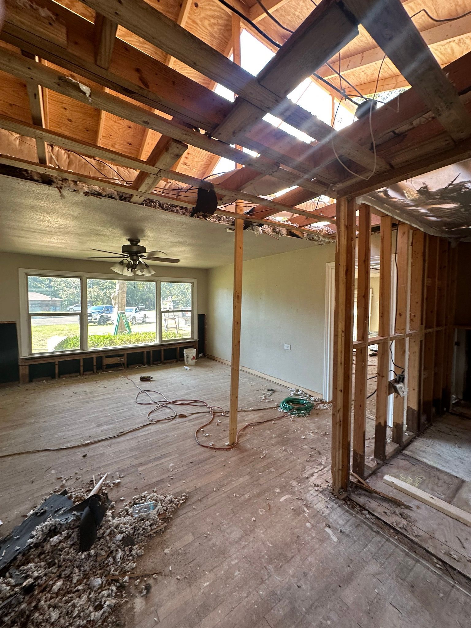 Interior of a house under renovation, with exposed roof beams, damaged ceiling, and unfinished walls.