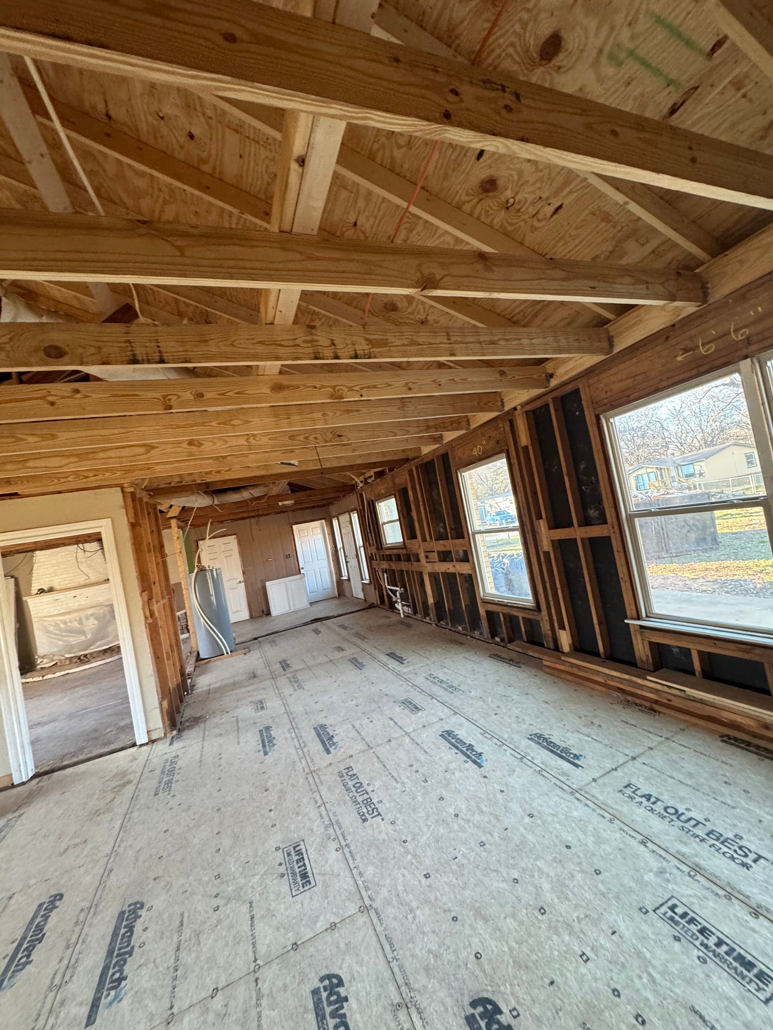 Unfinished interior of a wood-framed building with exposed trusses, open windows, and subflooring.