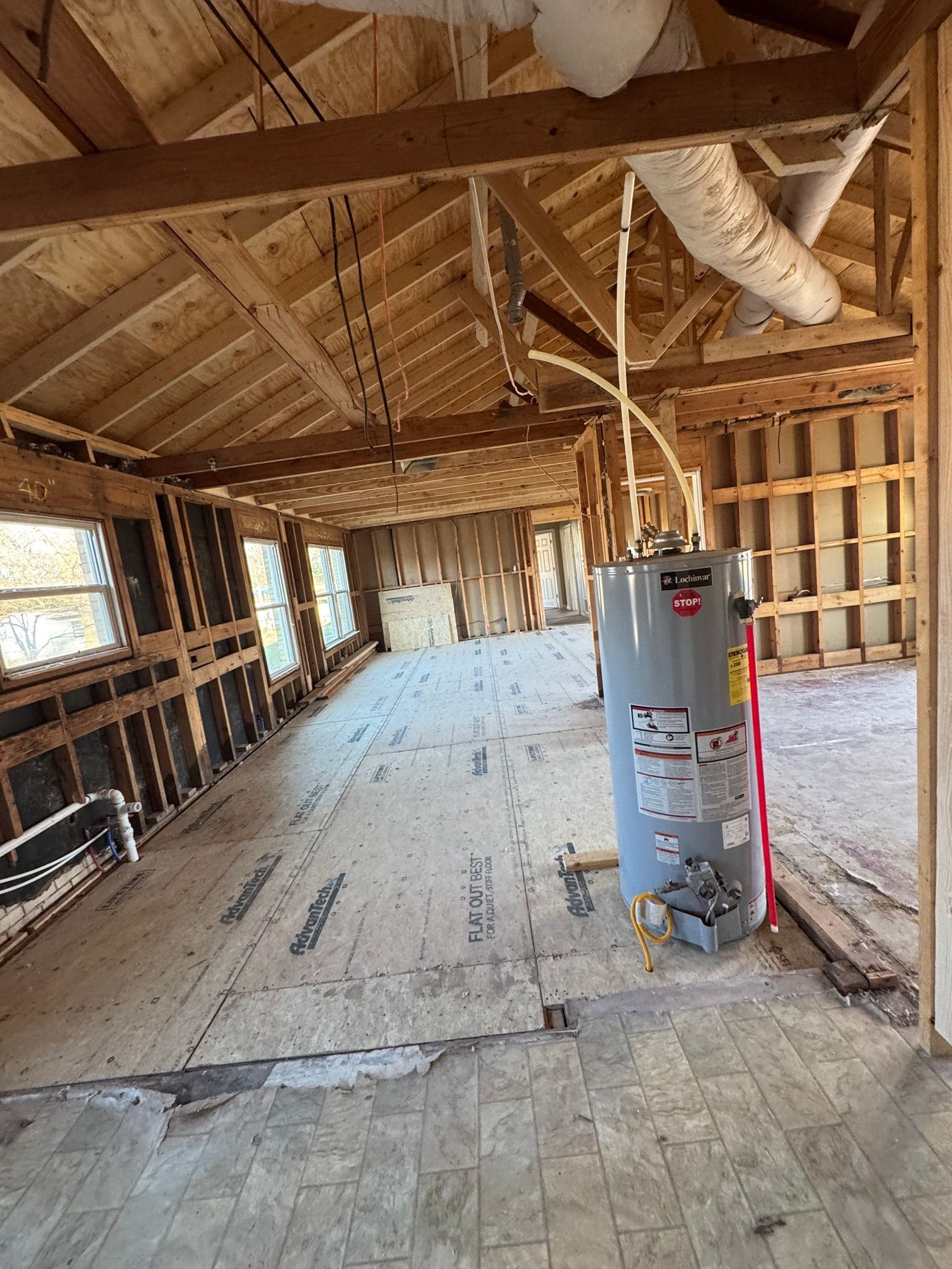 Unfinished attic interior with exposed rafters, insulation, windows, and a water heater on a plywood floor.