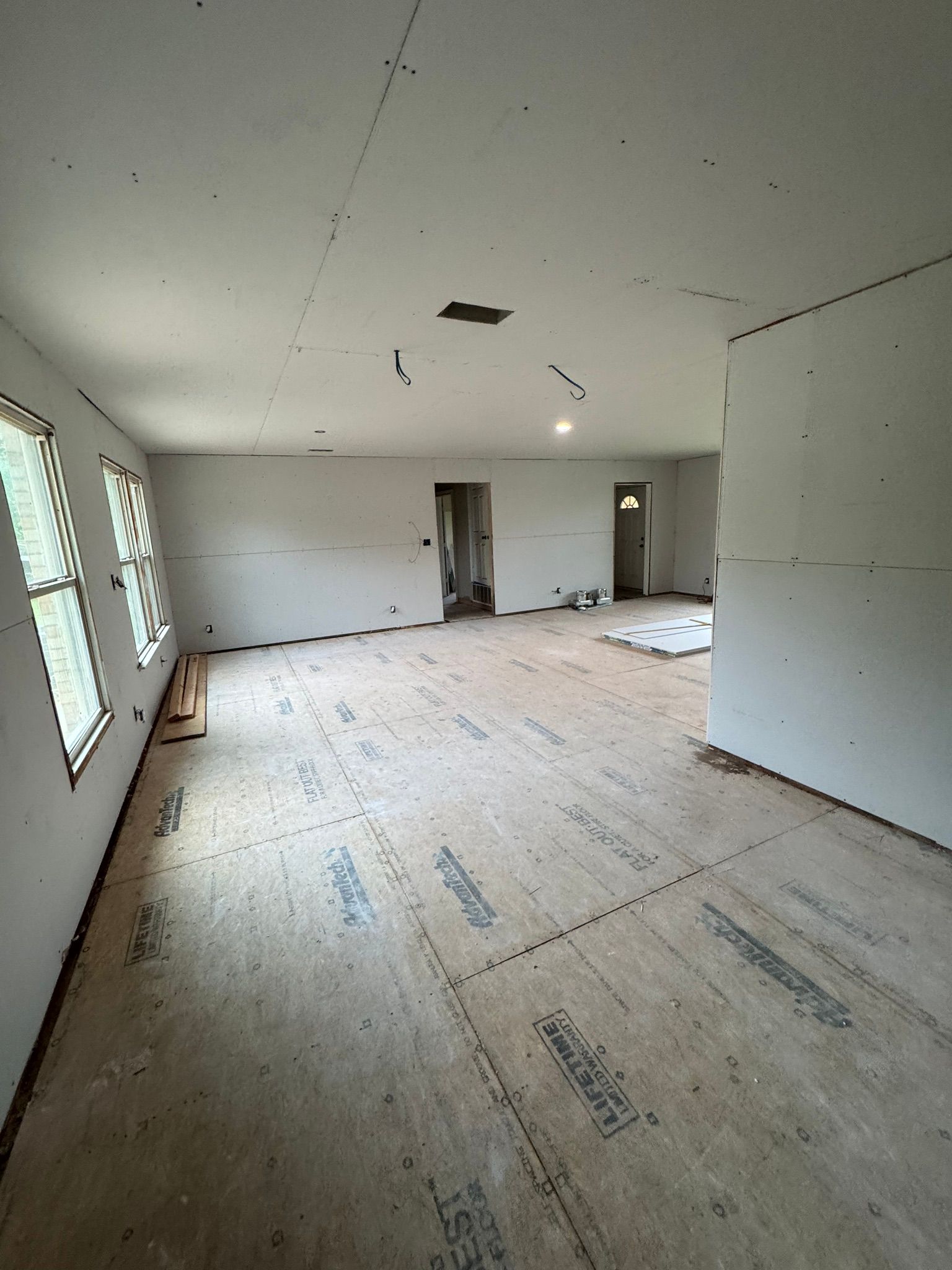 Empty unfinished room with white walls, bare floor, and large windows on the left.