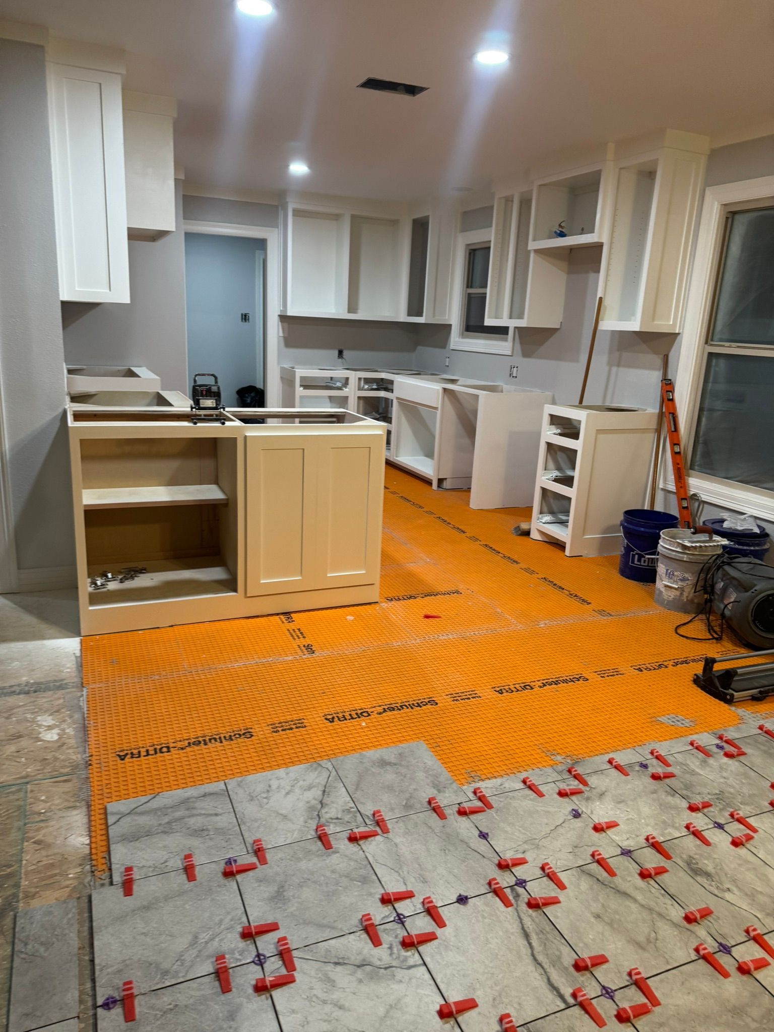 Renovated kitchen with white cabinets, orange protective floor covering, and tools during construction