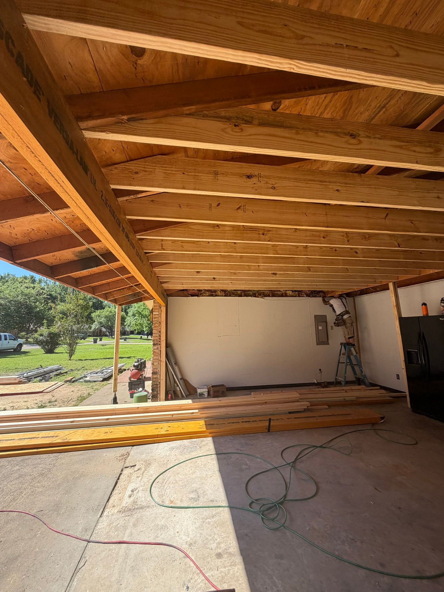 Open garage with exposed wooden rafters, concrete floor, and sunlight from the driveway.