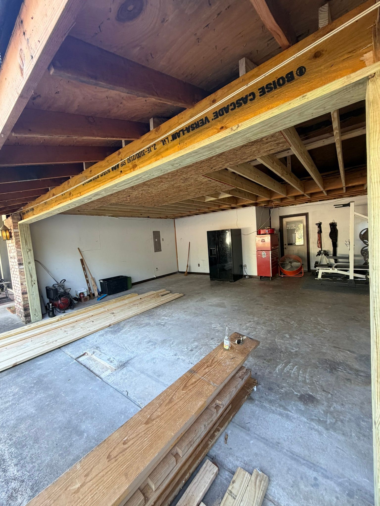Wide-angle view of an unfinished garage interior with exposed beams, concrete floor, and construction materials inside