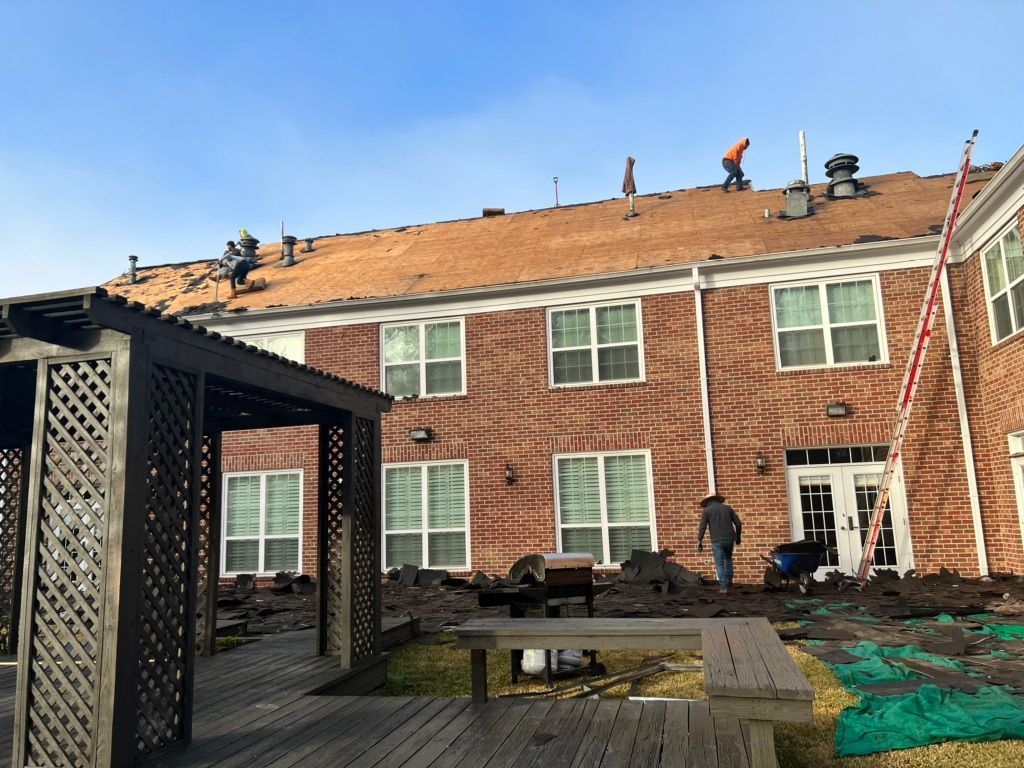 Backyard with workers repairing a two-story brick house roof and siding under a blue sky