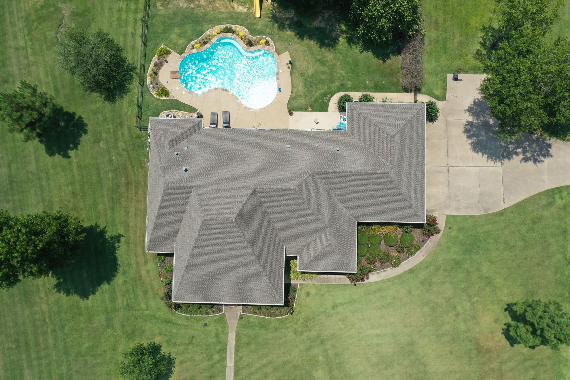 Aerial view of a suburban house with a backyard pool, lawn, and driveway