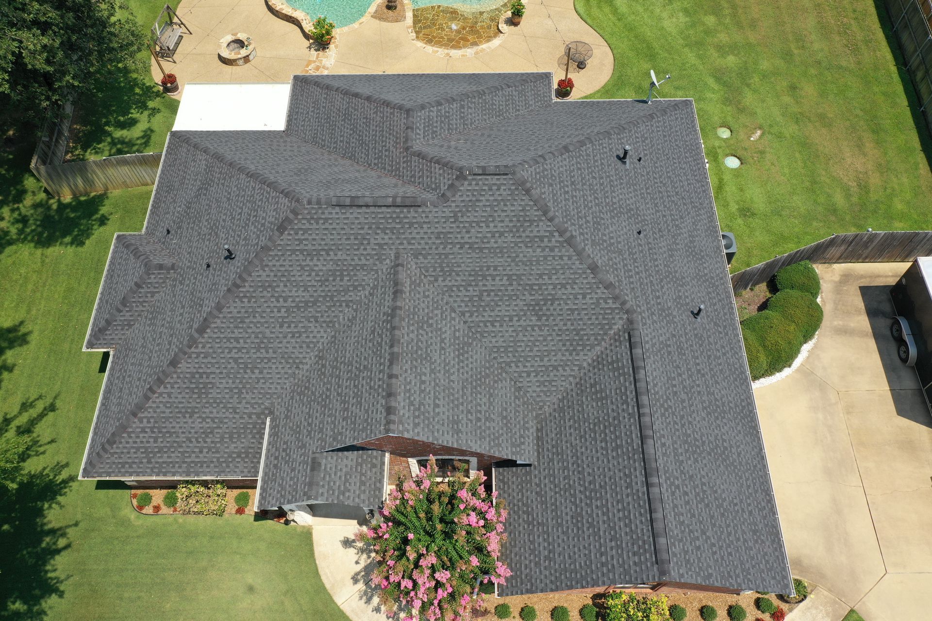 Aerial view of a house with a dark gray shingle roof, surrounded by lawn and a driveway.