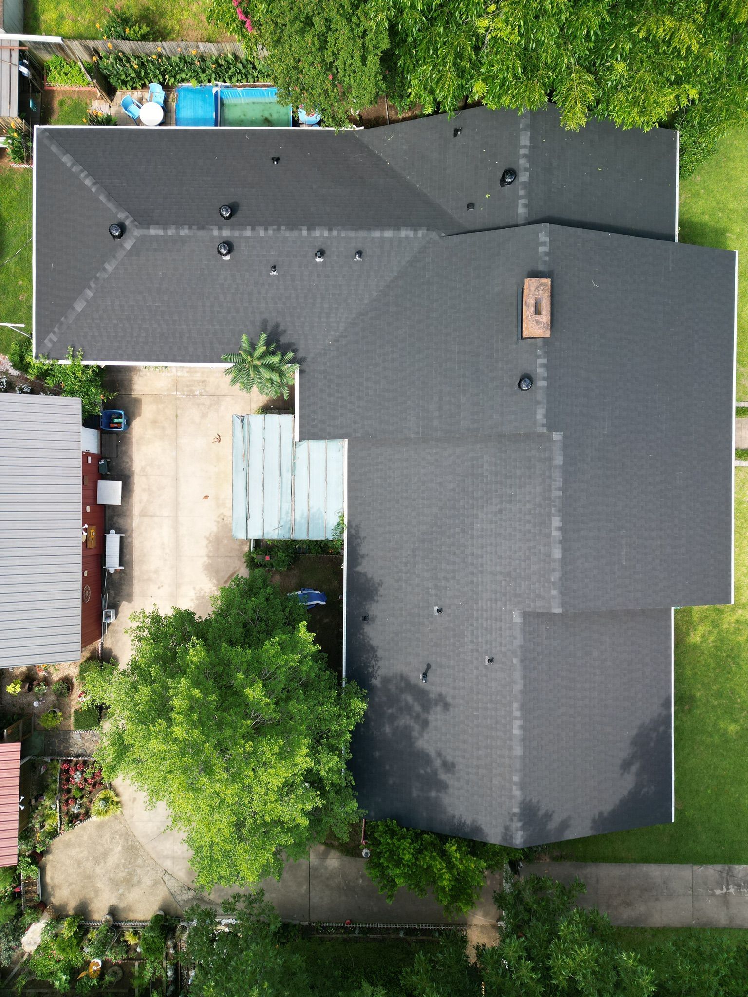 Aerial view of a dark gray house roof surrounded by trees and neighboring yards.