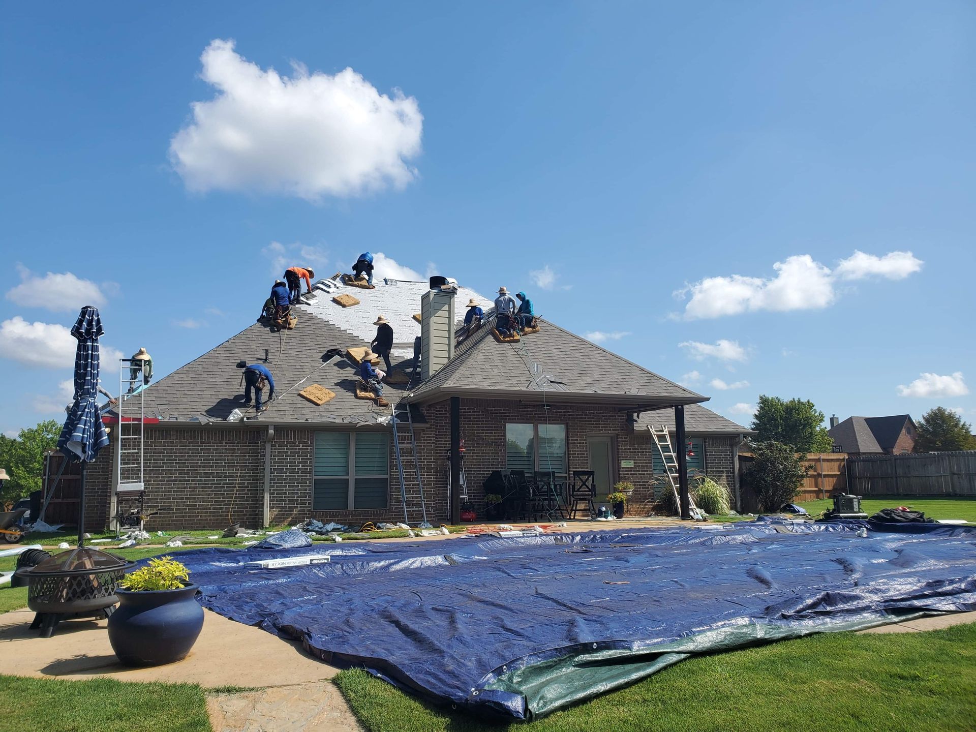 Workers repairing a house roof under a blue tarp on a sunny day