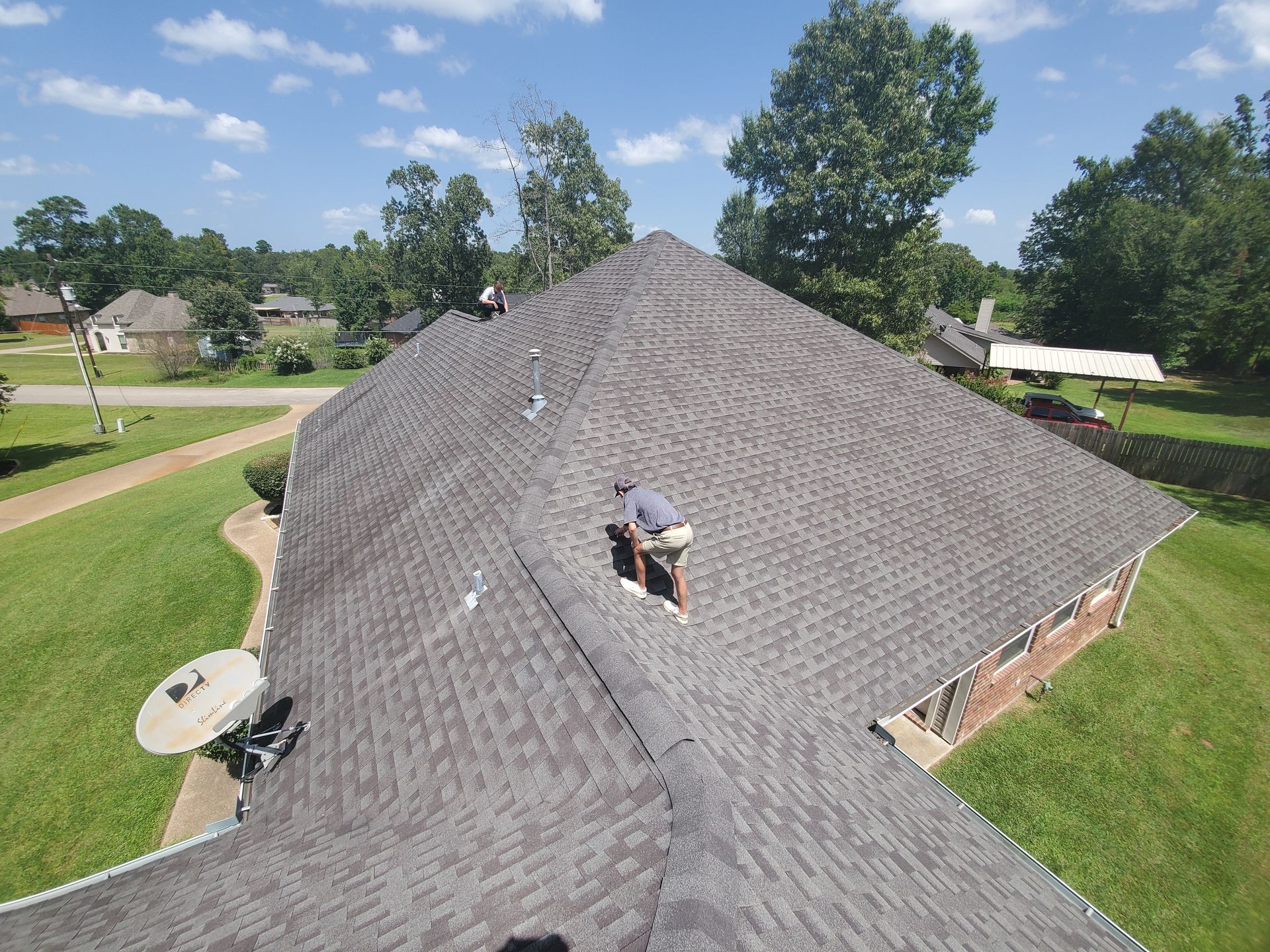 Roofing crew working on a shingled house roof in a suburban neighborhood