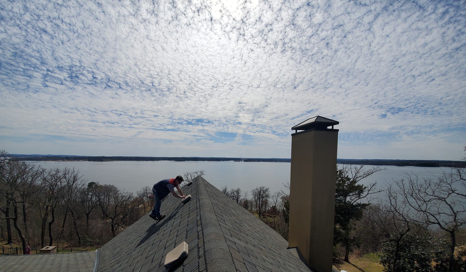 Worker on a rooftop near a chimney, with a cloudy sky and water in the background