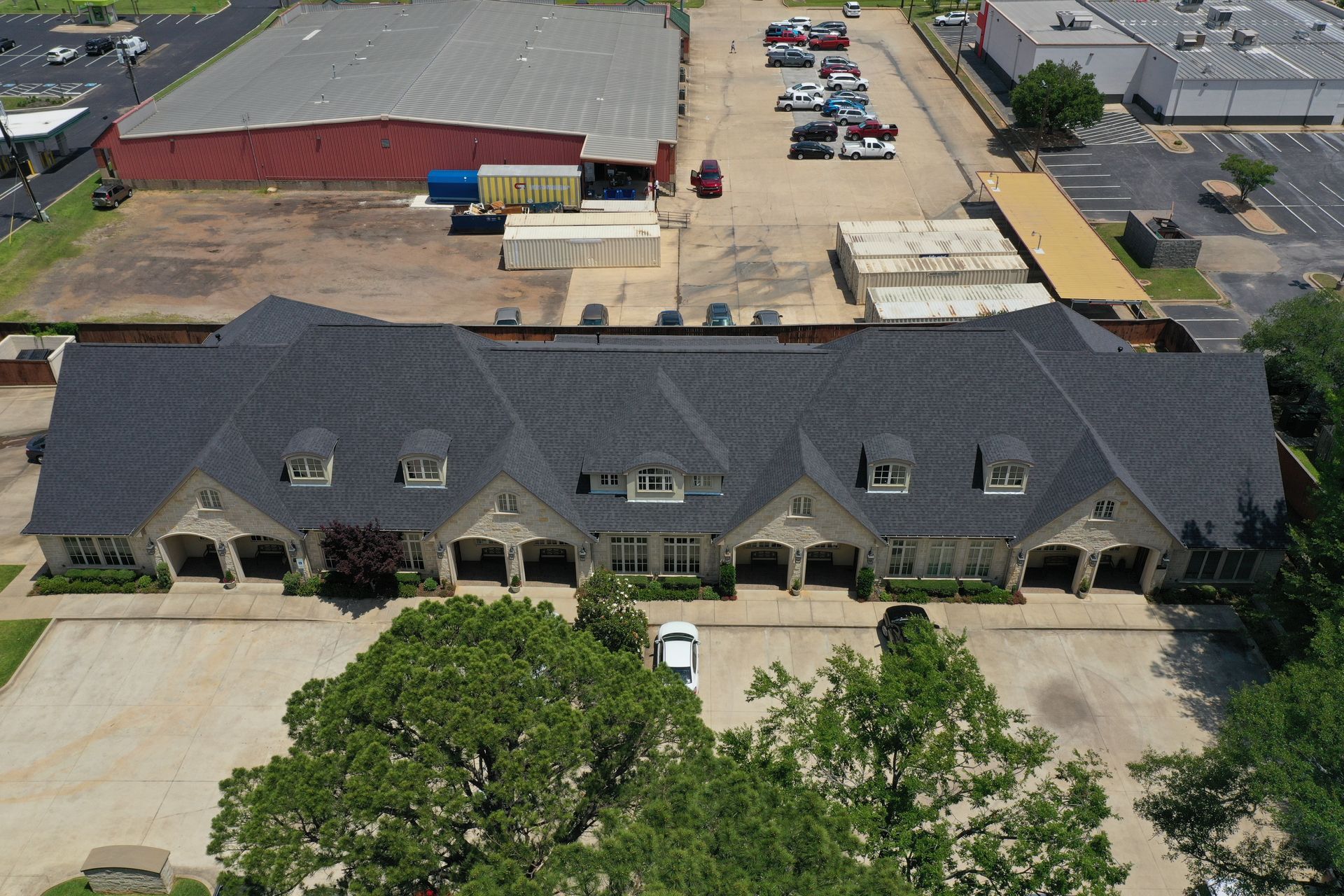 Aerial view of a large commercial building with a dark roof, parking lot, and surrounding industrial area.